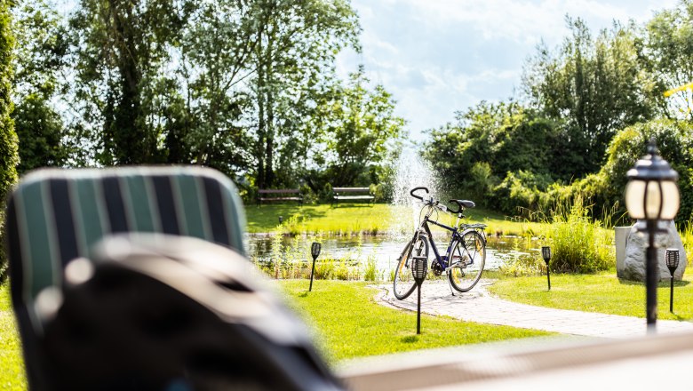 Garden, © Wiener Alpen / Martin Fülöp A bicycle is parked next to a pond with a fountain in a sunny garden.
