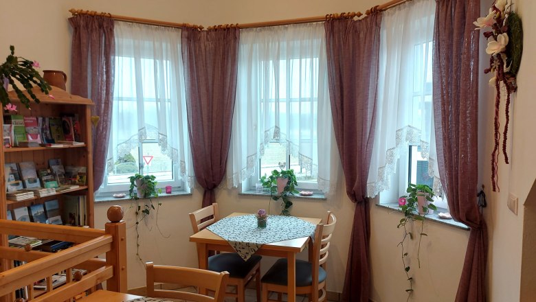 Breakfast room, © Trachsler A cozy breakfast room with wooden furniture, tablecloths and plants on the windowsills. Three windows with curtains let in daylight.