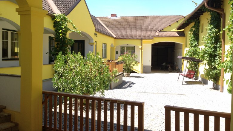Winzerhof & Guesthouse Greil, © M. Greil Inner courtyard of a yellow vineyard with plants and a swing.