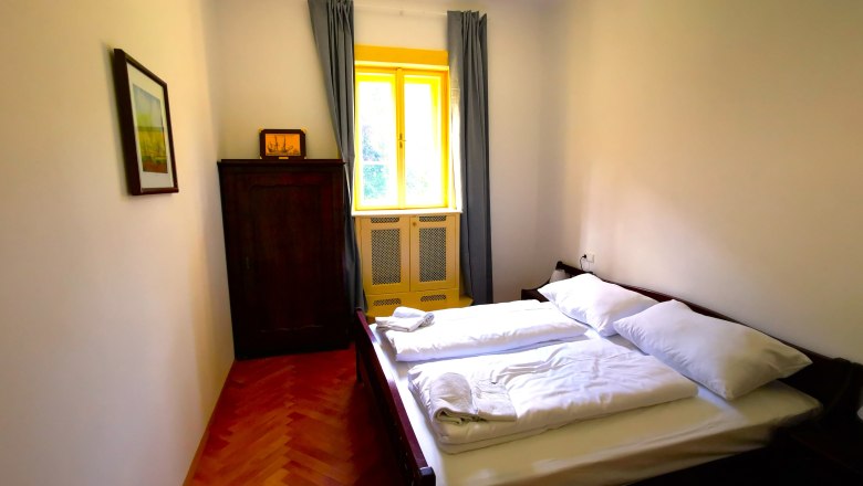 Bedroom in the Henriette apartment, © Herrnhof Bedroom with double bed, wardrobe and window with yellow frame.