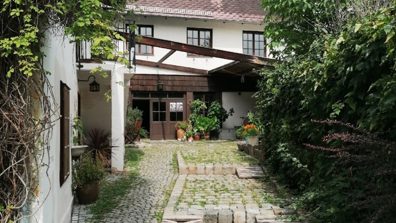 Courtyard entrance, © Gröger Paved courtyard entrance with plants and a white building in the background.