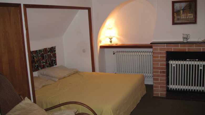 Bedroom, © Stein A cozy bedroom with a bed, an armchair, a lamp and a fireplace.