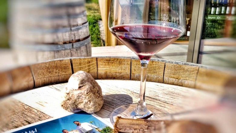 Weingarten.rocks - Terrace, © Weingarten.rocks A wine glass with red wine stands on a wooden table next to brochures and a stone.
