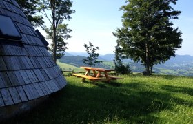 Sound garden, © Mostviertel Tourismus Wooden hut and picnic table on a meadow with trees and mountain views.