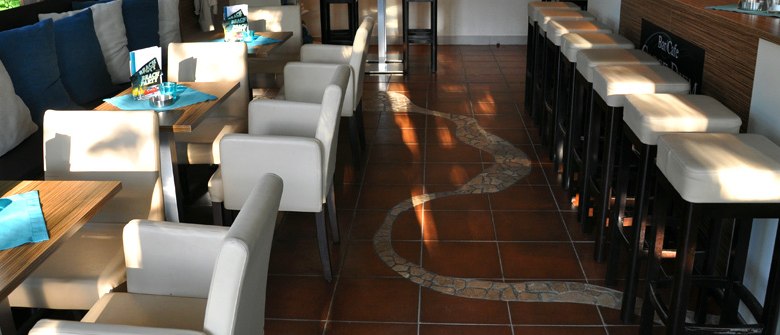 Carpe Diem_Interior view, © Carpe Diem Interior view of a café with white chairs and tables, brown tiled floor and bar stools.