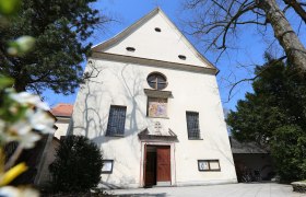 Capuchin Church, © schwarz-koenig.at Facade of the Capuchin church with entrance and windows, surrounded by trees.
