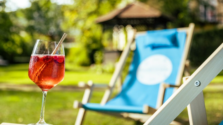 Pure summer freshness, © Wiener Alpen/Martin Fülöp A glass with a red drink and a straw on a deckchair in the garden.