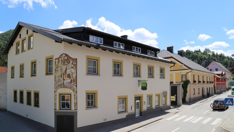 Pension Grasl, © Familie Grasl A yellow building with the sign 'Pension Grasl' on a street in sunny weather.