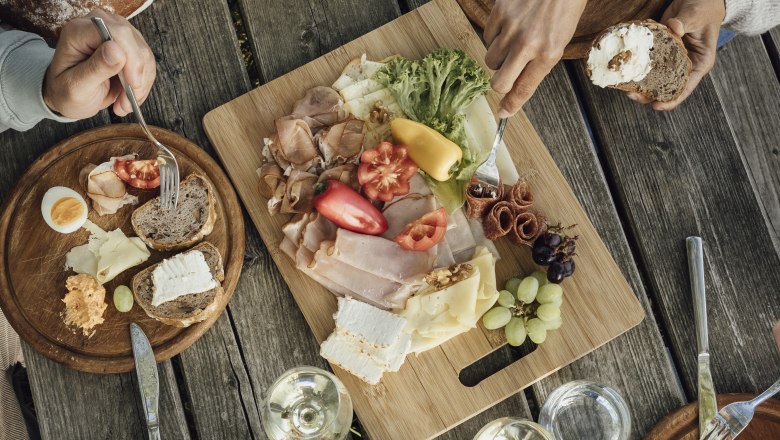 Heurigen snack, © Weinviertel Tourismus GmbH / Sophie Menegaldo A rustic wooden table with a snack of bread, cheese, cold cuts, vegetables and wine.