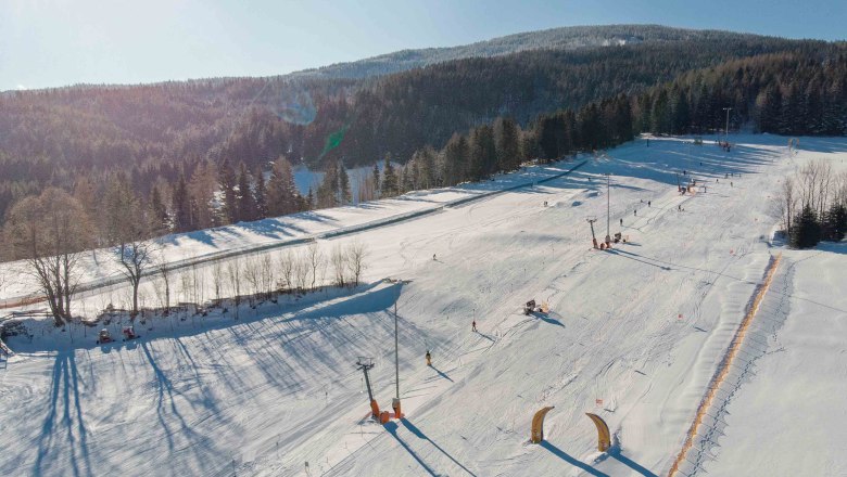 Family ski area at the Wexl Arena St. Corona am Wechsel, © Wexl Arena St. Corona am Wechsel Aerial view of a snow-covered ski resort with slopes and forest in the background.