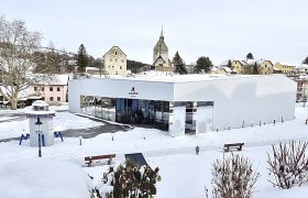Sconarium in winter, © Wiener Alpen Modern building in the snow with a church in the background.
