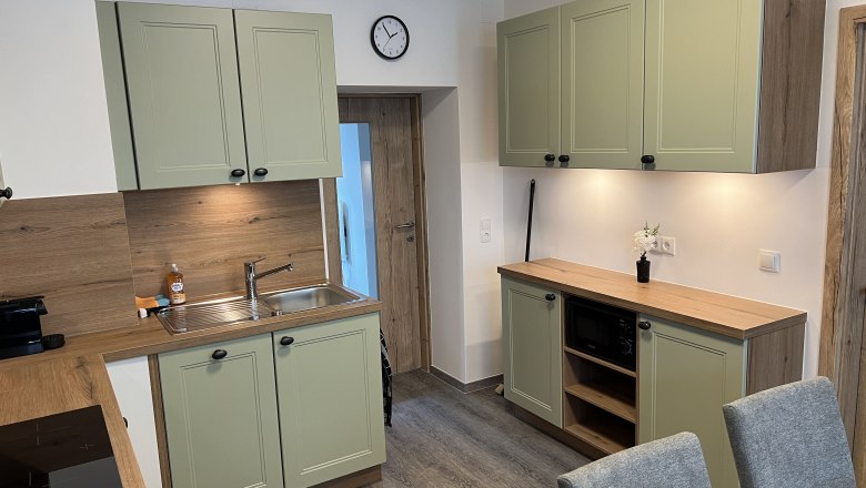 Kitchen vacation home Höflein, © Anton Sommer Modern kitchen with green cabinets, wooden worktops and gray chairs.