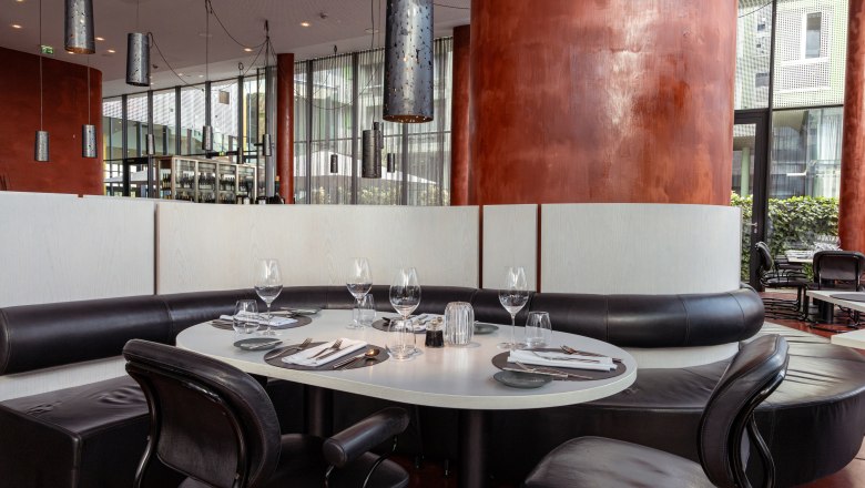 LOISIUM Langenlois, © Niederösterreich Werbung / Maximilian Pawlikowsky Modern restaurant with a table setting, black leather seats and large red columns.