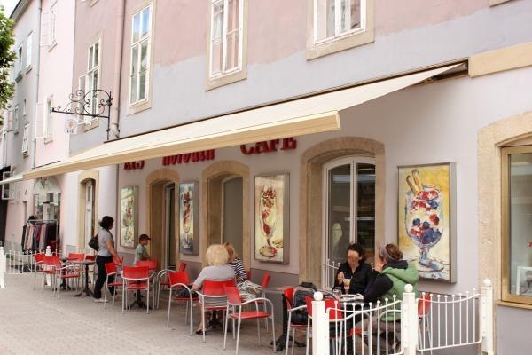 Ice cream JuditH Café Konditorei, © Eis JuditH Café Konditorei Exterior view of the café with red chairs and guests at tables.
