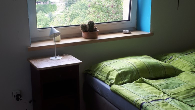 Room, © DB A bedroom with a bed, a bedside table and a window overlooking a green landscape.