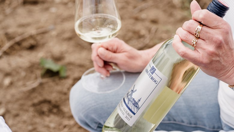Winery Ladentrog, © Stefan Jurecek Person holding a bottle of white wine and a wine glass.