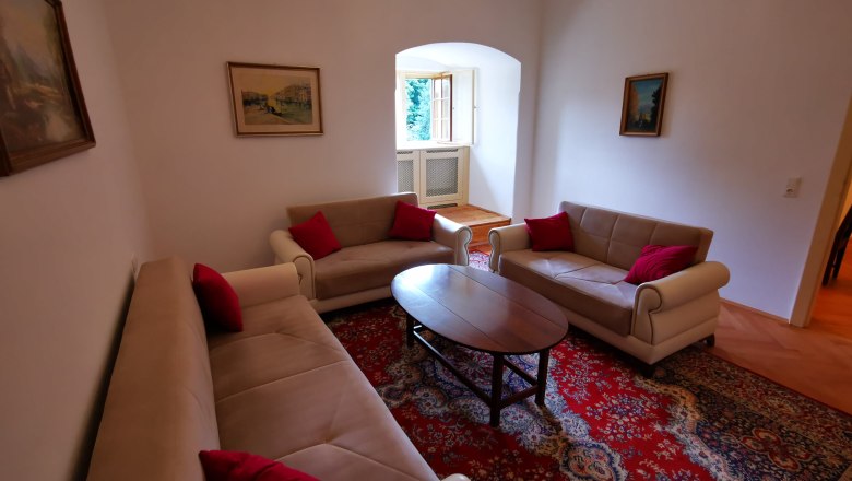 Living room in apartment Josef, © Herrnhof Living room with three sofas, red carpet and paintings on the walls.