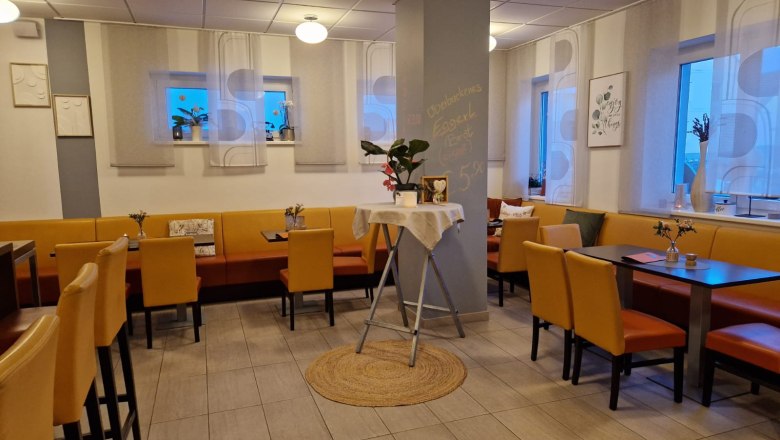 Café Eggerl, © Café Eggerl Interior view of a cozy café with yellow chairs and tables, decorated with plants and pictures on the walls.