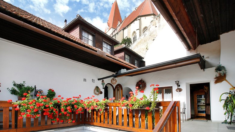 Cozy, quiet terrace, © Annemarie Heller A terrace with red flowers, a wooden fence and a view of a building with a church tower.