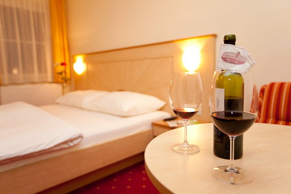 Seminar room, © Christian Fürnholzer A cozy hotel room with a double bed, two wine glasses and a bottle of wine on a table.