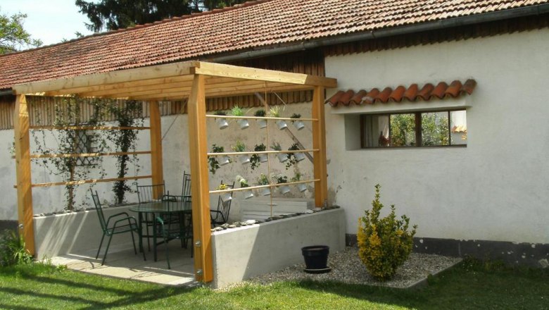 Country house Rossatz, © Familie Schlager A garden with a wooden pergola, including a table and chairs. In the background a building with a tiled roof.