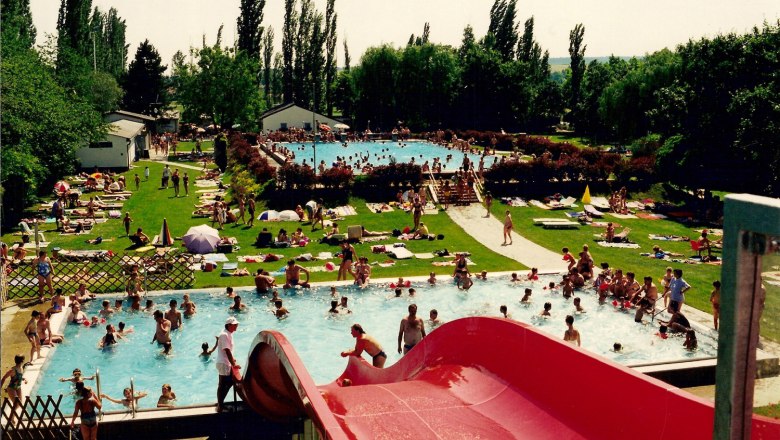 Outdoor pool, © Gemeinde Neusiedl/ Zaya Outdoor pool with lots of people in the water and on the sunbathing lawn, red slide in the foreground.