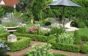Garden Weinpension Andrea, © Weinpension Andrea Familie Schwertführer A well-tended garden with flower beds, a parasol and seating area.