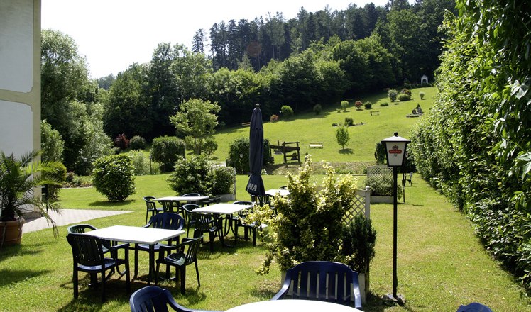 Garden, © Das Steinberger Garden with tables and chairs, surrounded by trees and meadows.