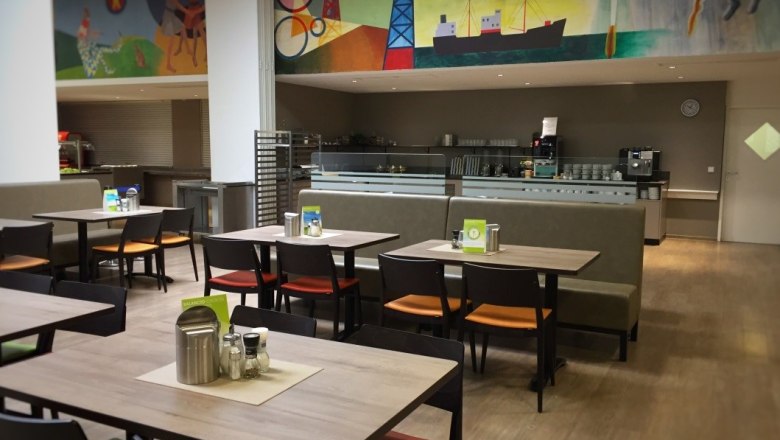 Restaurant, © Stadthotel Hollabrunn Interior view of a restaurant with empty tables and chairs, colorful wall painting in the background.