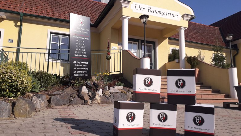 Exterior view of the Baumgartner, © Der Baumgartner Exterior view of a yellow building with the inscription 'Der-Baumgartner'. In front of the entrance are cardboard boxes with the logo 'BJ'.