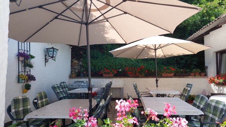 TDR-Pension Welserhof, © Bartfai Cozy outdoor area with tables, chairs and parasols, surrounded by flowers and plants.