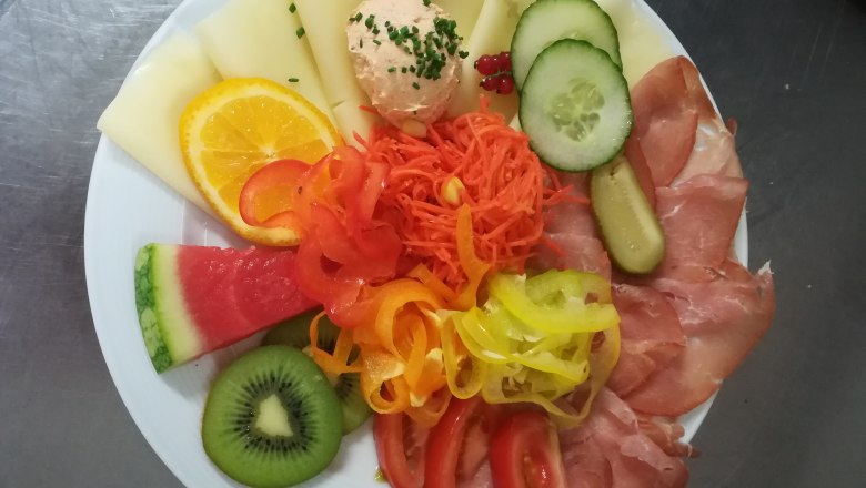 heurigenjause-family-resch-2, © Familie Resch A plate with cheese, ham, vegetables and fruit, including melon, kiwi, cucumber and peppers.