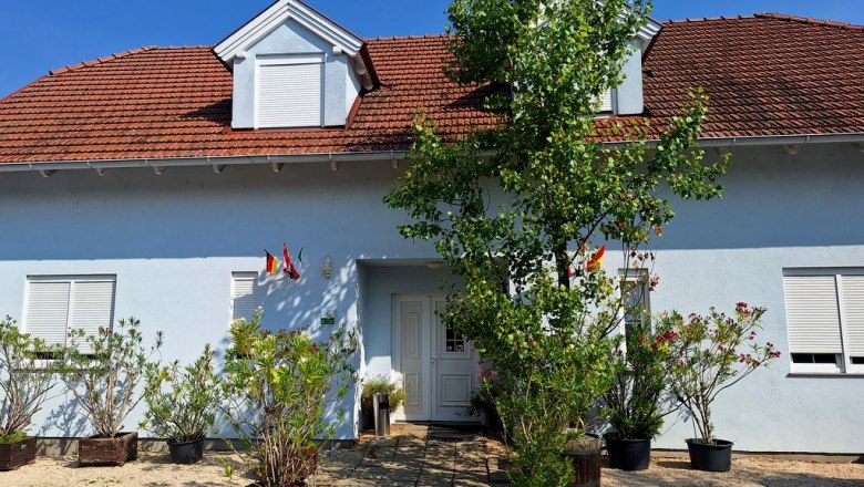 Cozy bed and breakfast, © Fam. Windisch A light blue house with a red roof and plants in the foreground.