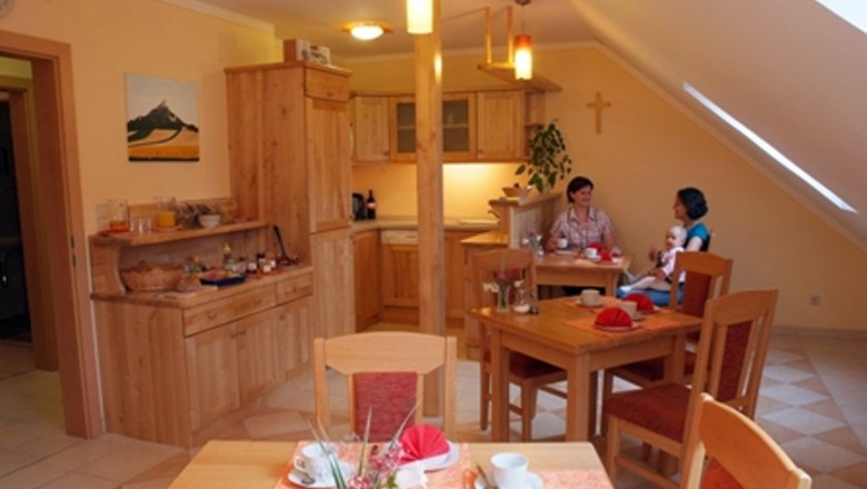 Breakfast room, © Seymannfilm A cozy breakfast room with wooden furniture, laid tables and two people chatting. A child is sitting on one person's lap.