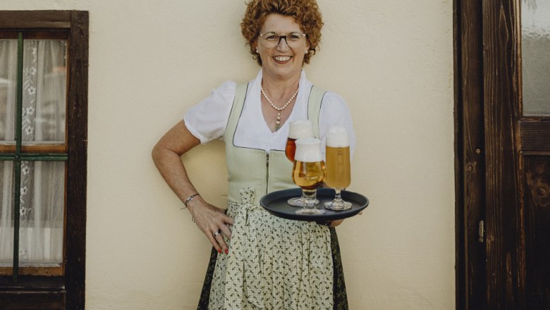 Landlady Silvia Beisteiner, © Niederösterreich Werbung/Sophie Menegaldo Woman in traditional dress with tray full of beer glasses in front of a wall.