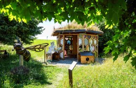 Bee pavilion in the bee park Klein-Pöchlarn, © Robert Herbst A bee pavilion with a grass roof and bee figures in the Klein-Pöchlarn Bee Park, surrounded by green nature.