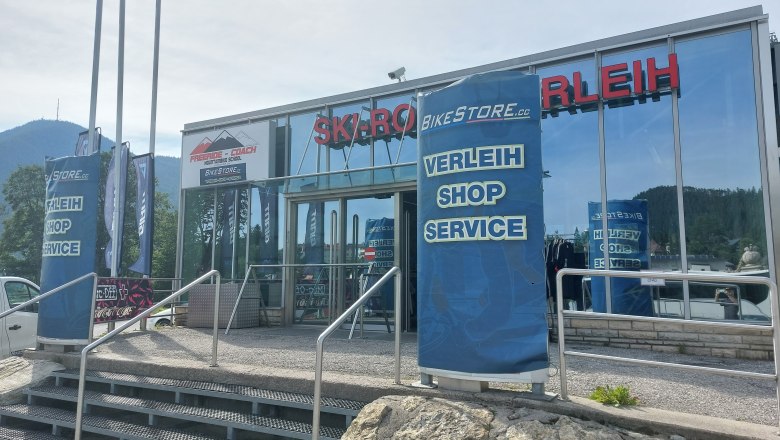 Bikestore.cc, © Bikestore.cc Entrance to a sports store with rental, store and service. Mountains in the background.