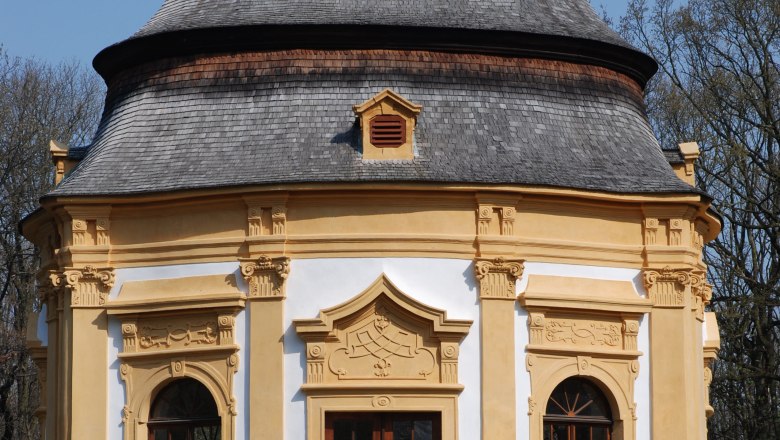 Garden pavilion, © Gemeinde Obersiebenbrunn Baroque garden pavilion with yellow decorations and a gray roof against a blue sky.