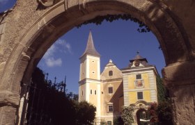 Mühlbach Castle, © Schloss Mühlbach Historic building with tower seen through a stone archway.
