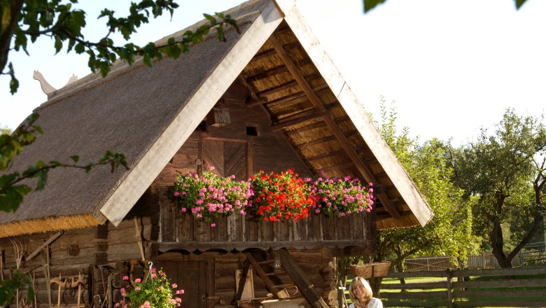Troadkasten in the Lanzenkirchen Farmers' Museum, © Haberler, Foto Tschank Traditional wooden building with thatched roof and flowers, woman and child in traditional costume in front.