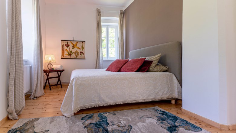 Old post office bedroom view, © Aumüller Caroline Bedroom with bed, red cushions, carpet and window with curtains.