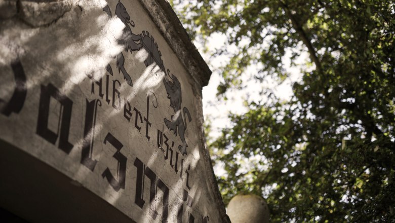 Foam mill, © K. Vyhnalek Close-up of an old building with lettering and coat of arms, surrounded by trees.