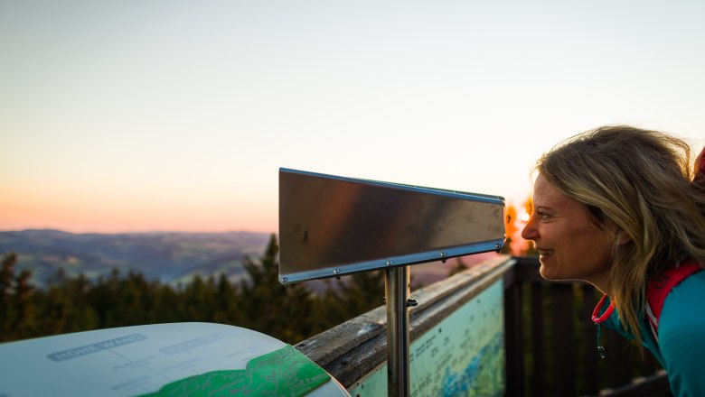 View through the Vienna Alps Viewer, © Wiener Alpen/Martin Fülöp Woman looking through a telescope at a viewpoint at sunset.