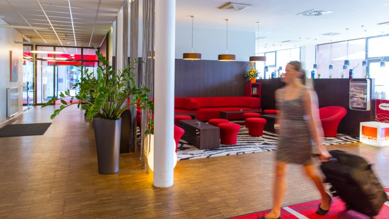 Lobby, © arte Hotel Krems Hotel lobby with red sofa and woman with suitcase.