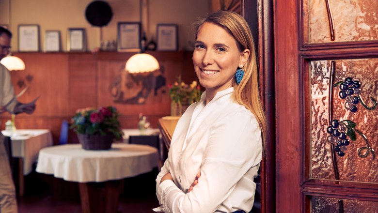 Landlady Vera Baumgartlinger, © Niederösterreich Werbung/Andreas Hofer Woman in a white shirt smiles in a traditional restaurant with wooden furnishings.