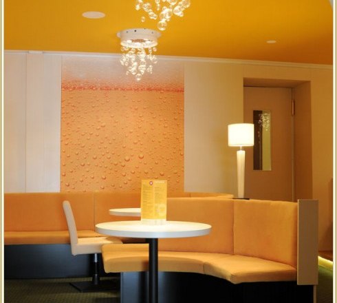 Café-Pub Rathaus interior view, © Café-Pub Rathaus Interior view of a modern café with yellow walls, round tables and upholstered benches.