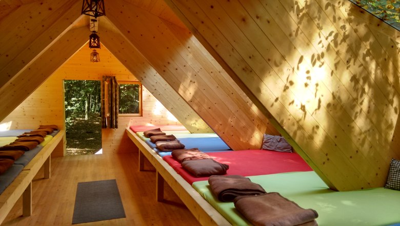 Forest camp, © Ochys Interior view of a wooden hut dormitory with mattresses and blankets.