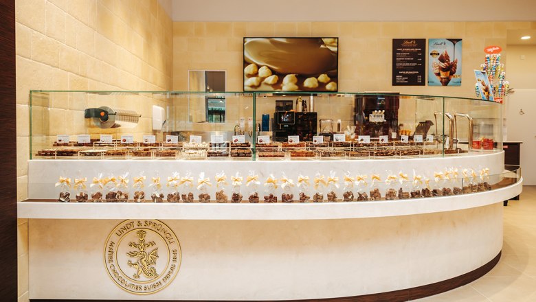 Chocolate selection, © Philipp Lipiarski Interior view of a chocolate store with chocolates in glass display cases and a Lindt & Sprüngli logo.