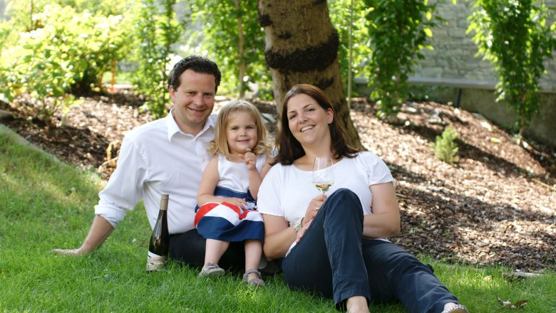Benedikt Winery, © Benedikt Family sitting in a meadow under a tree with a bottle of wine and a glass.