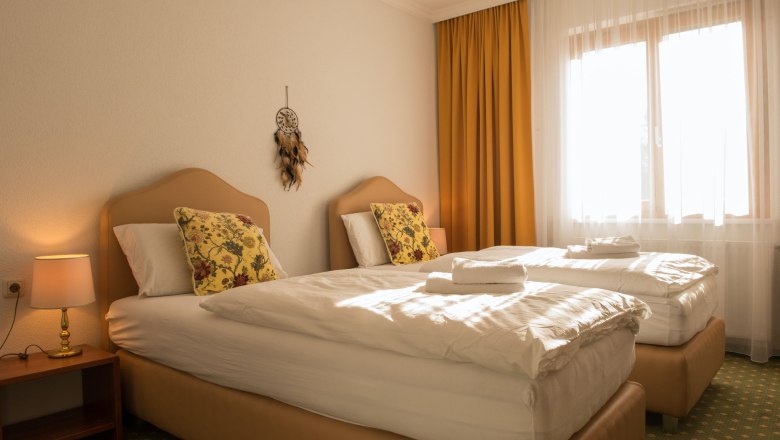 Double room 24, © Dorfschmiede eG A cozy double room with two single beds, yellow curtains and a dream catcher on the wall.